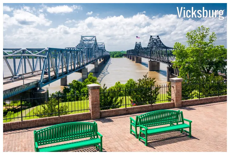 Twin bridges across the large Mississippi River at Vicksburg, Mississippi, and green benches in the waterfront walk street