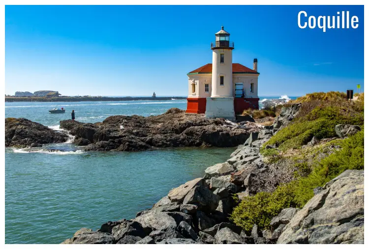 Massive rocks in the water below the tall Bandon Lighthouse along the calm river in Coquille, Oregon