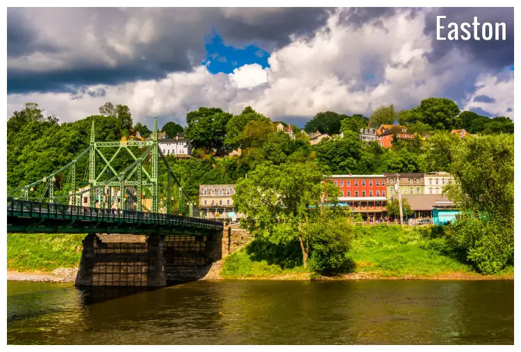 A golden shot of the green Northampton Street Bridge crossing over the Delaware River in Easton, Pennsylvania, colorful homes amid trees across the river