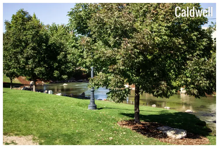 A small, calm river flows via a scenic nature park full of trees in the city of Caldwell, Idaho