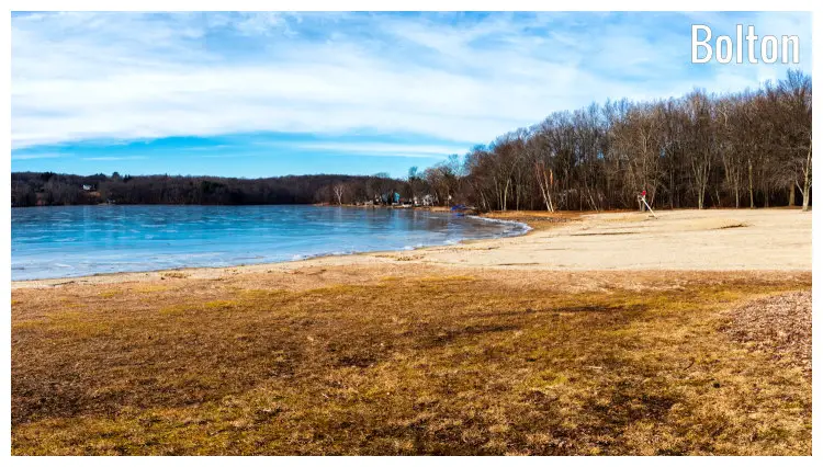 Grass, brown sand, and trees on an empty beach in Bolton, Connecticut, overlooking the blue waters far out