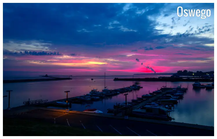 The colorful sun rising over a calm marina in Oswego, New York, with a view of numerous boats and yachts docked along several piers