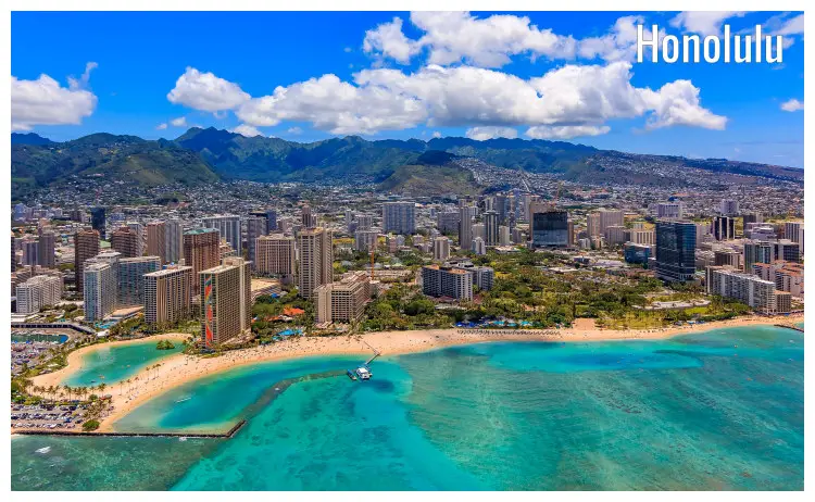 Waikiki beach with clear calm waters on the foot of Honolulu city, Hawaii, with the vast cityscape and mountains in the distance Waikiki beach with clear calm waters on the foot of Honolulu city, Hawaii, with the vast cityscape and mountains in the distance