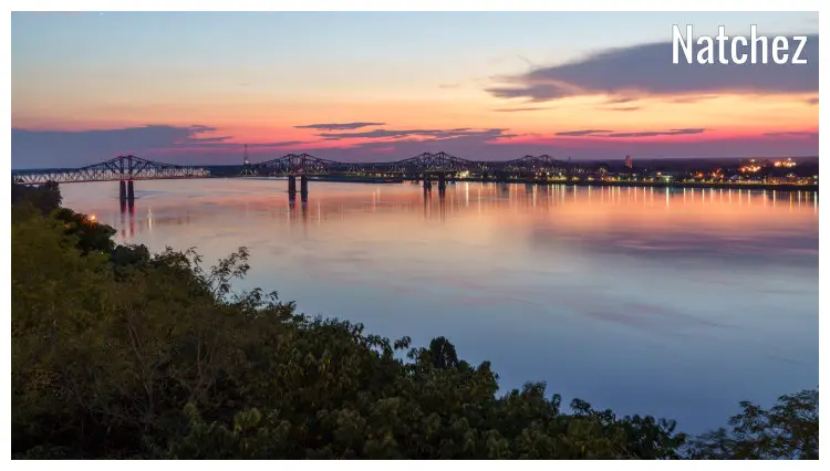 A long bridge over the Mississippi River in Natchez, seen with the colorful sunset sky in a nice mirror image in the river water