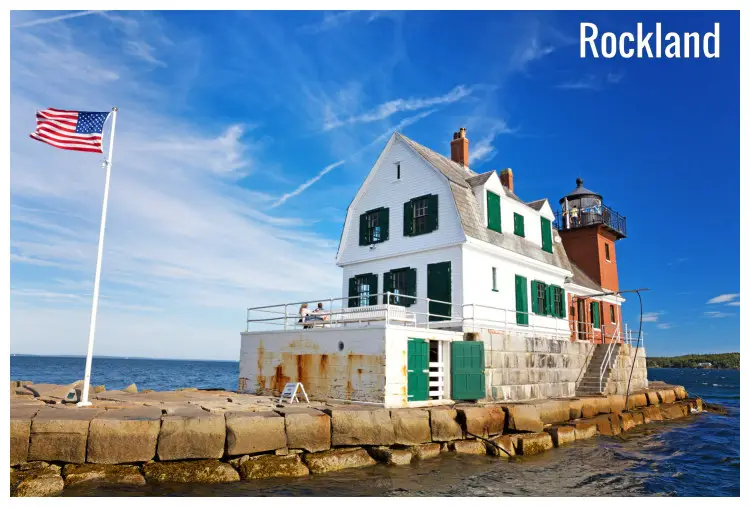 A US flag flying outside a lighthouse on the water in Rockland, Maine