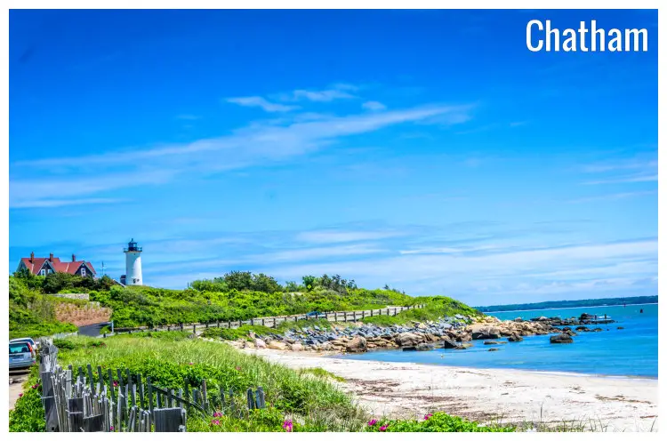The calm blue water and white sand on a typical beach in Cape Cod, with a visible path and a far view of the high Chatham Lighthouse, Massachusetts