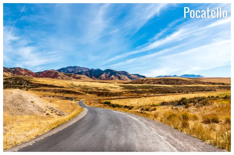 A clear, winding road in the hilly landscape leading to Pocatello, Idaho, with scenic mountains seen in the distance