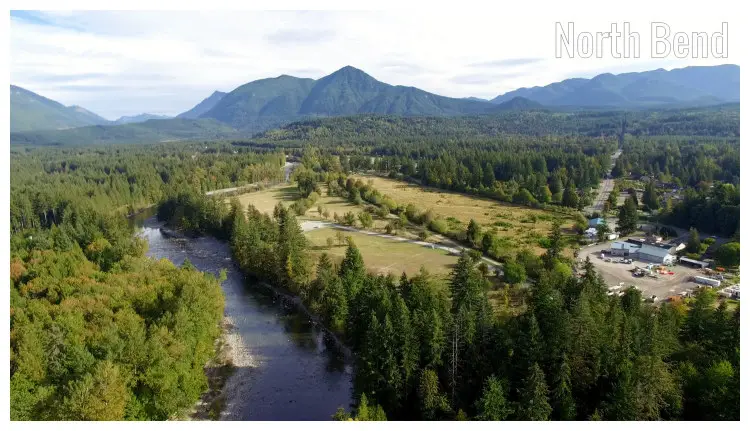A panorama of the Snoqualmie River with homes, green trees on either side, and a far view of the Preacher Mountain ranges in North Bend, Washington A panorama of the Snoqualmie River with homes, green trees on either side, and a far view of the Preacher Mountain ranges in North Bend, Washington