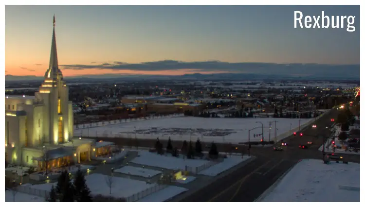 The crossroads near a large lit temple in Rexburg, Idaho, with a view of the rest of the city and a colorful, cloudy sunset sky on the horizon