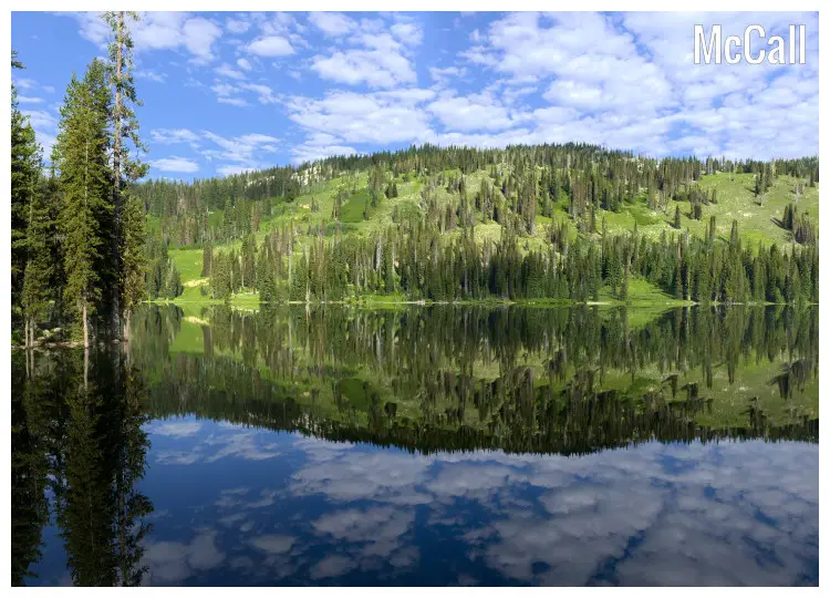 The hilly landscape full of scenic pine trees as well as the bright cloudy sky above in a great mirror image in the Goose Lake in McCall, Idaho The hilly landscape full of scenic pine trees as well as the bright cloudy sky above in a great mirror image in the Goose Lake in McCall, Idaho
