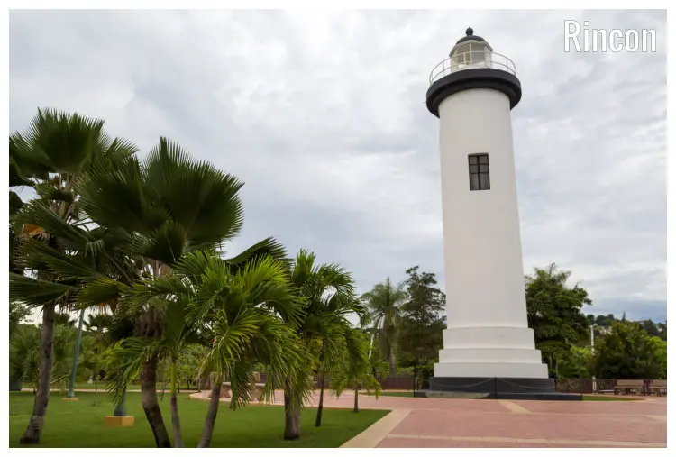 A tall and white lighthouse in the scenic palm trees and well-done field lawns in the Rincon City within the Puerto Rico Harbor A tall and white lighthouse in the scenic palm trees and well-done field lawns in the Rincon City within the Puerto Rico Harbor