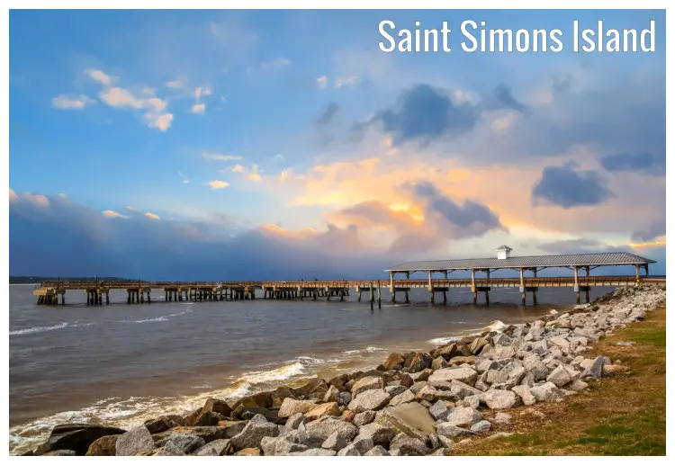 A long pier with a large shed on the St. Simons Island, Georgia, the rocks and seawater and colorful sunset clouds in the sky above