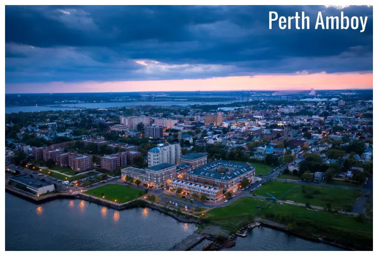 A scenic panorama of Perth Amboy Town in New Jersey, with the bright neon lights as the sun sets behind the colorful and heavy cloudy sky above