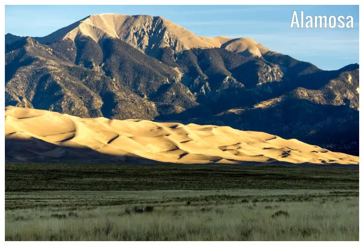 A vast field near the iconic dune field in Alamosa, Colorado, with a back view of the vast brown sandy dune hotbed and distant mountain ranges A vast field near the iconic dune field in Alamosa, Colorado, with a back view of the vast brown sandy dune hotbed and distant mountain ranges