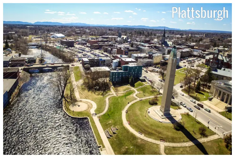 A sunny and dry day in the townscape of Plattsburgh, New York, with a view of the iconic tower next to the river, dry trees, and a hilly landscape view