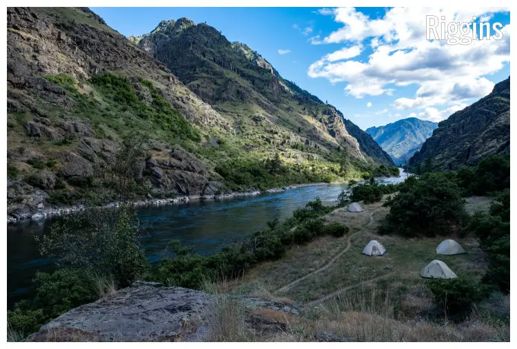 The scenic Snake River between large mountains, with pitched tents and visible footpaths in the mountains near Riggins, Idaho