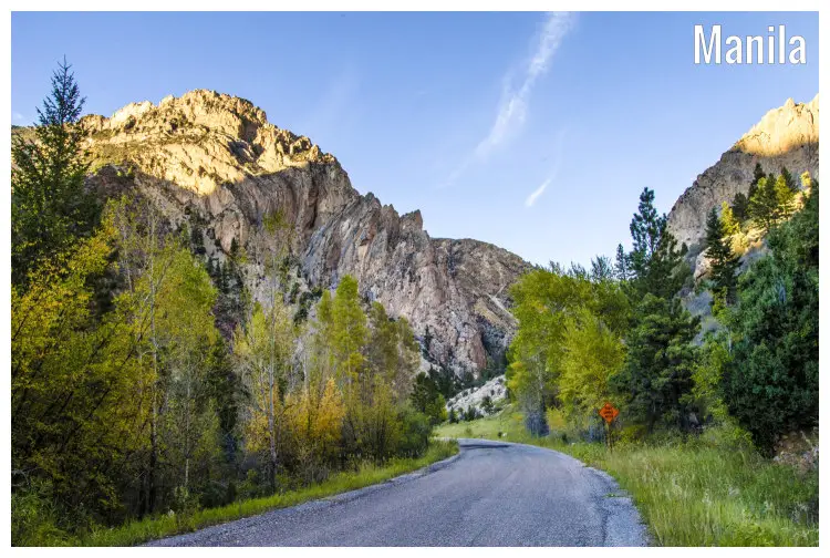 Trees and a snaky road passing on the foot of rocky hills in the mountain region of Manila, Utah