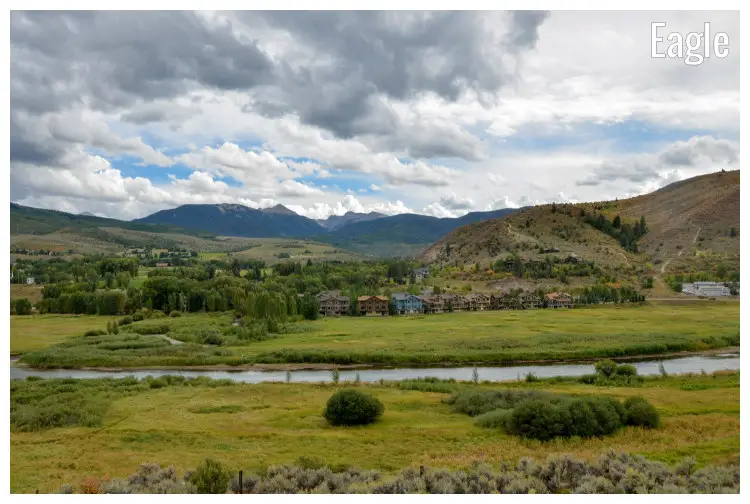 The snaky Eagle River flows through fields and a small town afar at the base of the Rocky Mountains in Eagle, Colorado The snaky Eagle River flows through fields and a small town afar at the base of the Rocky Mountains in Eagle, Colorado