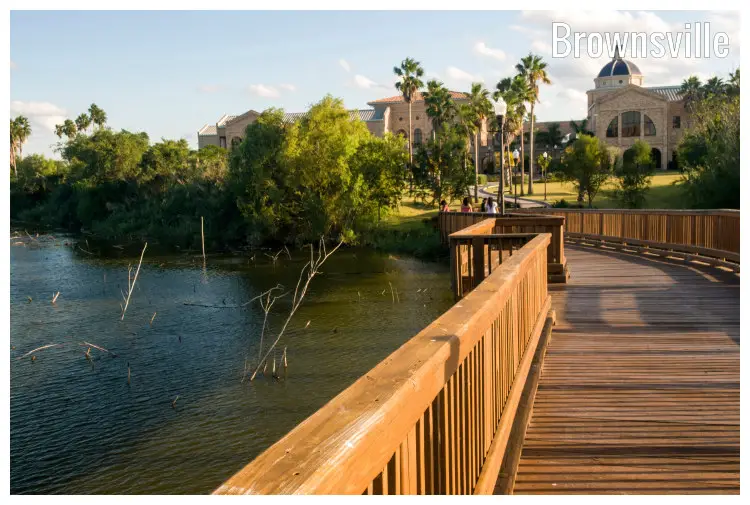 A wooden footbridge over a large river with beautiful houses and scenic fields on the other end, located near Brownsville in Texas A wooden footbridge over a large river with beautiful houses and scenic fields on the other end, located near Brownsville in Texas