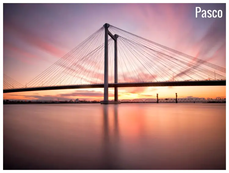 The pink sunrise sky over the iconic Pasco Bridge across the glassy calm waters near Pasco, Washington The pink sunrise sky over the iconic Pasco Bridge across the glassy calm waters near Pasco, Washington