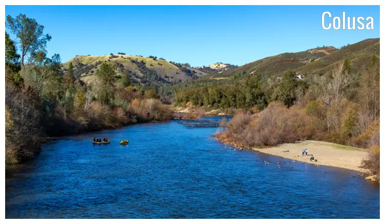 The scenic setting of shrubs, forests, and a boat on the stunning blue waters of the Colusa River in California The scenic setting of shrubs, forests, and a boat on the stunning blue waters of the Colusa River in California