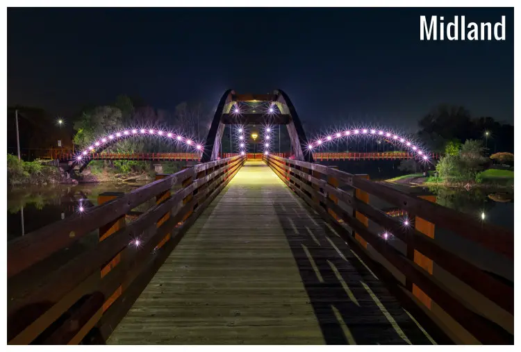 A footwalk along the Tridge facing lit arches on the bridges on either side crossing the iconic Chippewa and Tittabawassee Rivers in Midland, Michigan