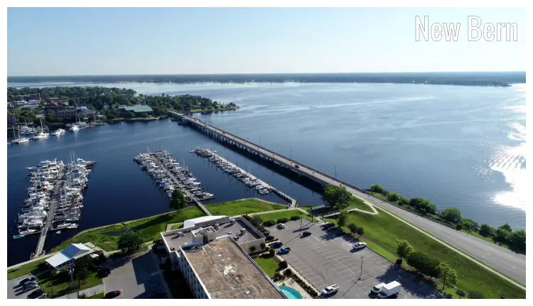 Boats and yachts docked along several piers in New Bern, North Carolina, with a view of a long and high bridge nearby, massive seascape and horizon