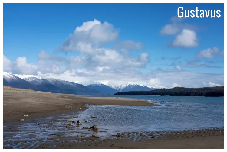 Brown sand and water on a section of the Gustavus Beach, Alaska, and snow-peaked mountains in the far view