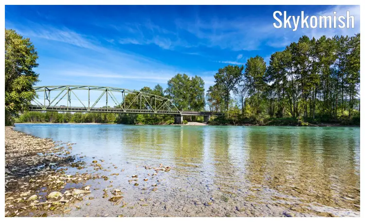 A calm Skykomish river with clear waters, visible stones, with a view of the iconic Lewis Street Bridge, near Monroe in Washington
